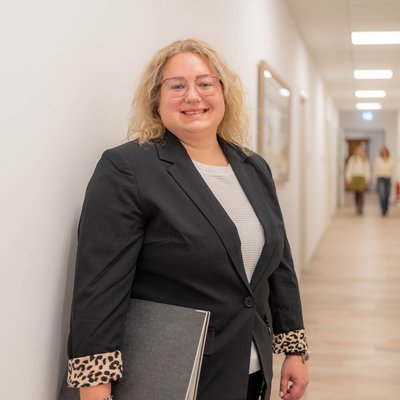 Beraterin steht im Flur und schaut lächelnd in die Kamera