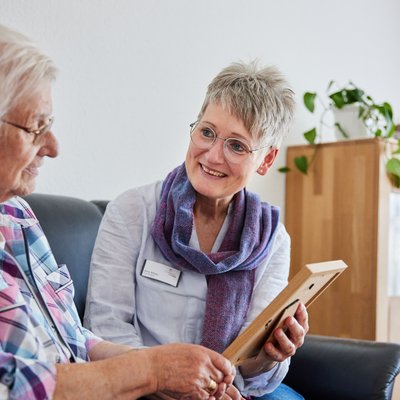 Mitarbeiterin hält Foto in der Hand und schaut es sich mit Betroffener an