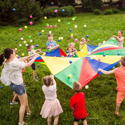 Kinder und Erzieherin haltet großes Fangtuch in die Luft und fangen Bälle