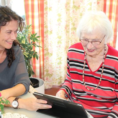 Betreuerin erklärt Bewohnerin etwas am Tablet